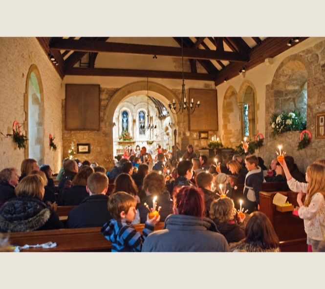 Families holding lit Christingles during a church service